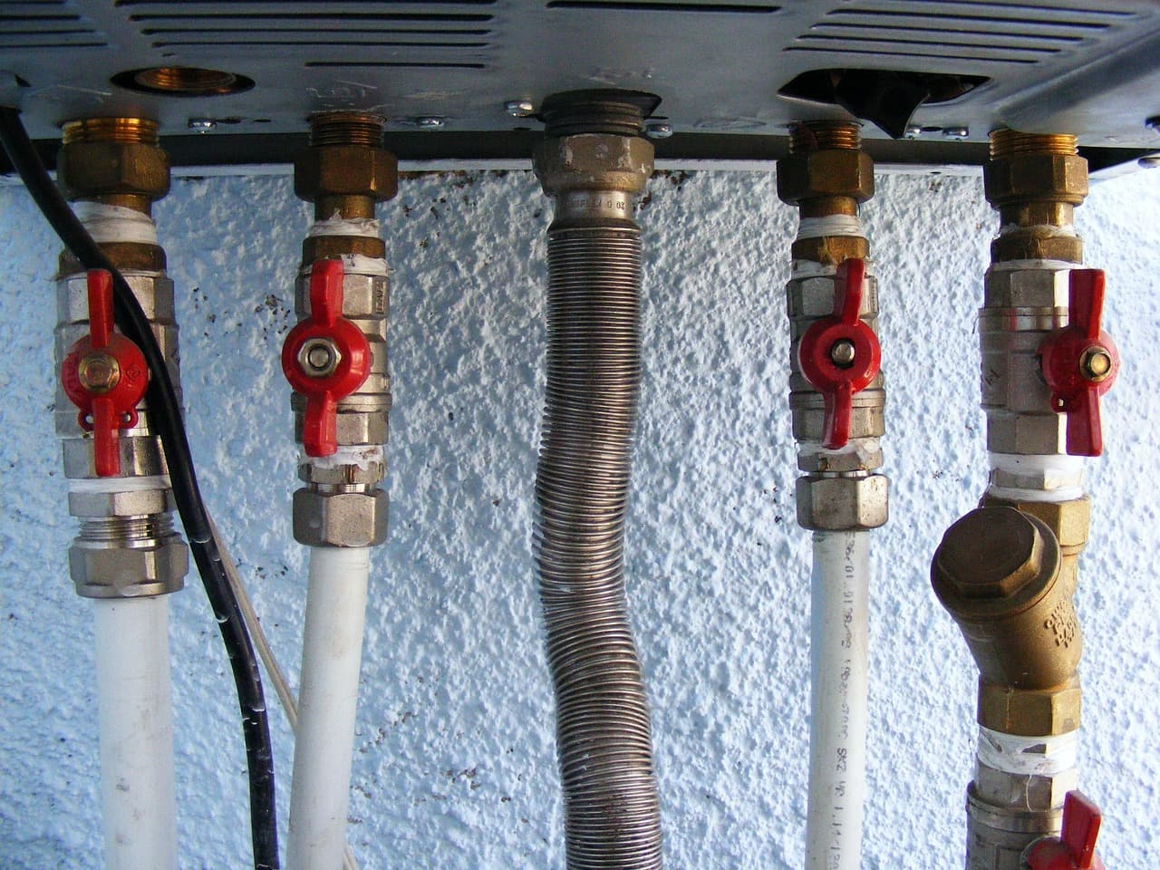 Valves and pipework underneath a wall-mounted boiler
